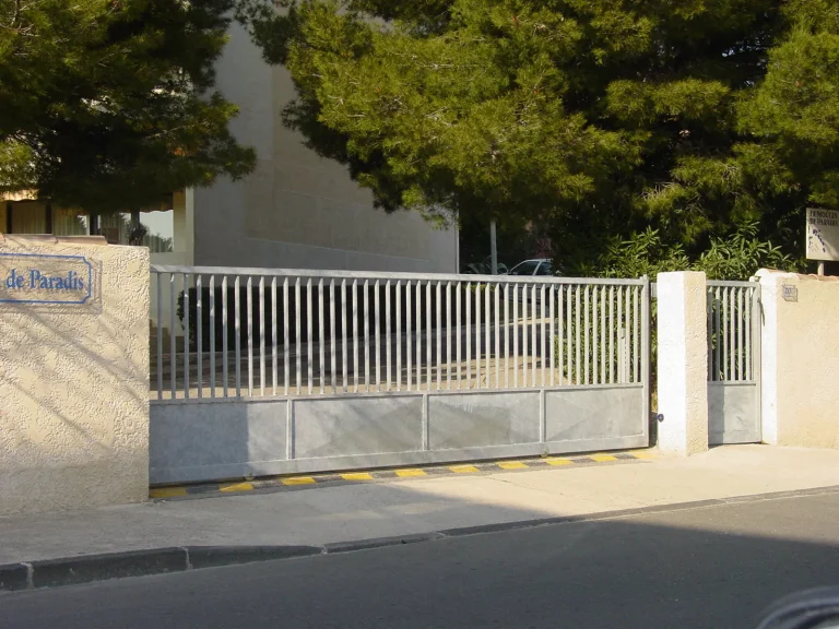 Entrée d'une copropriété équipée d'un grand portail et portillon en fer